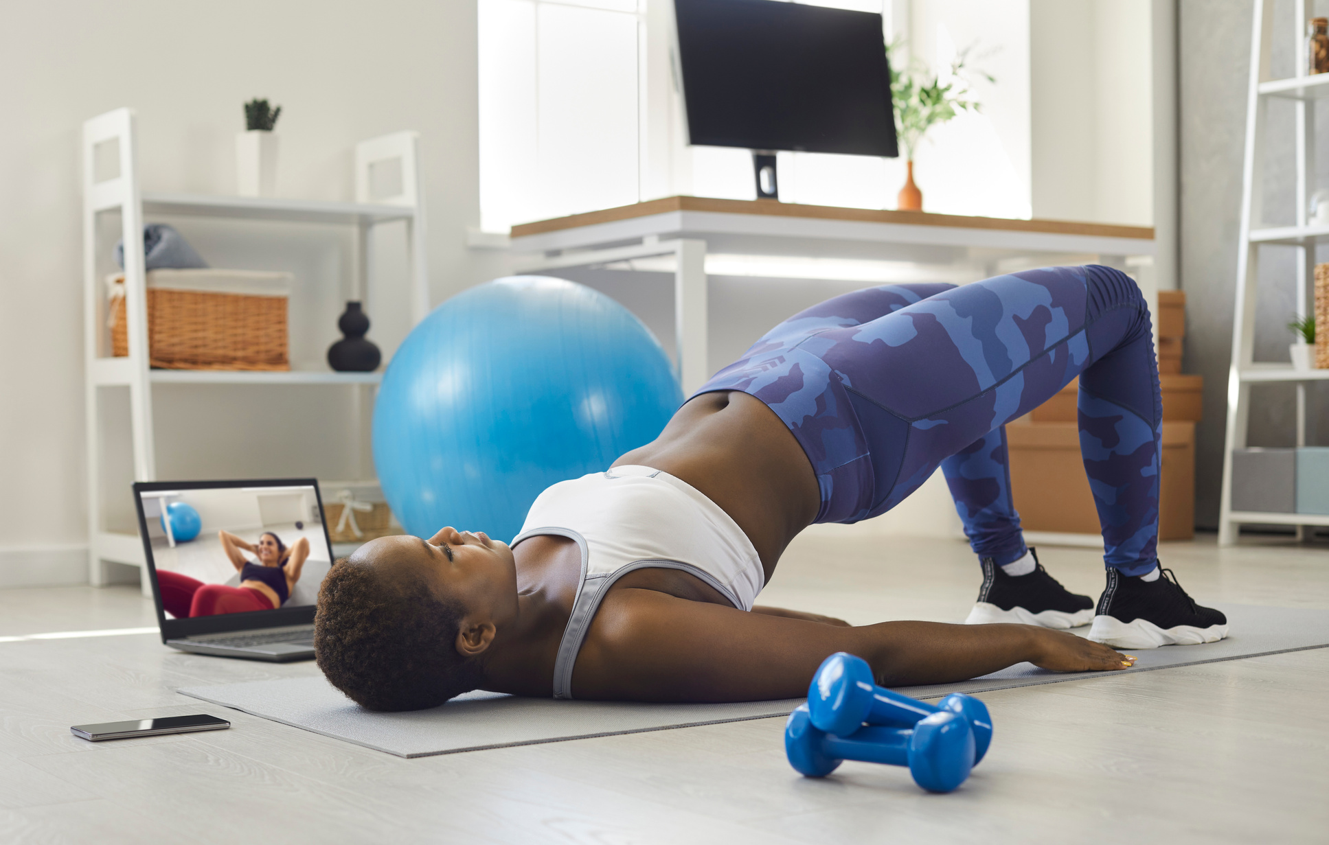 Black Woman Watching Sports Workout Video and Doing Glute Bridge Exercise at Home